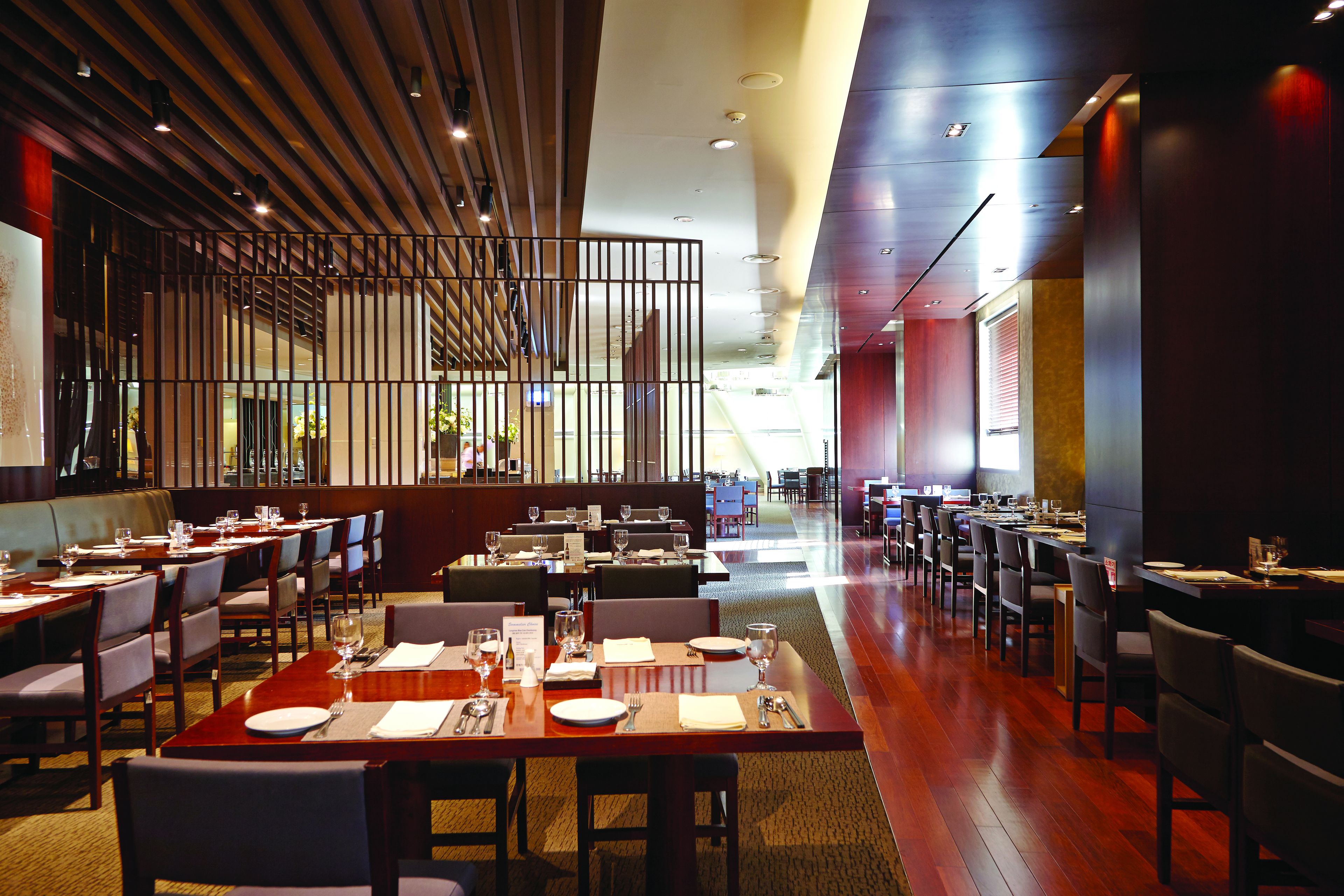 A modern restaurant with multiple dining tables and booths, wooden flooring, and a contemporary ceiling design.