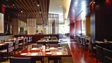 A modern restaurant with multiple dining tables and booths, wooden flooring, and a contemporary ceiling design.