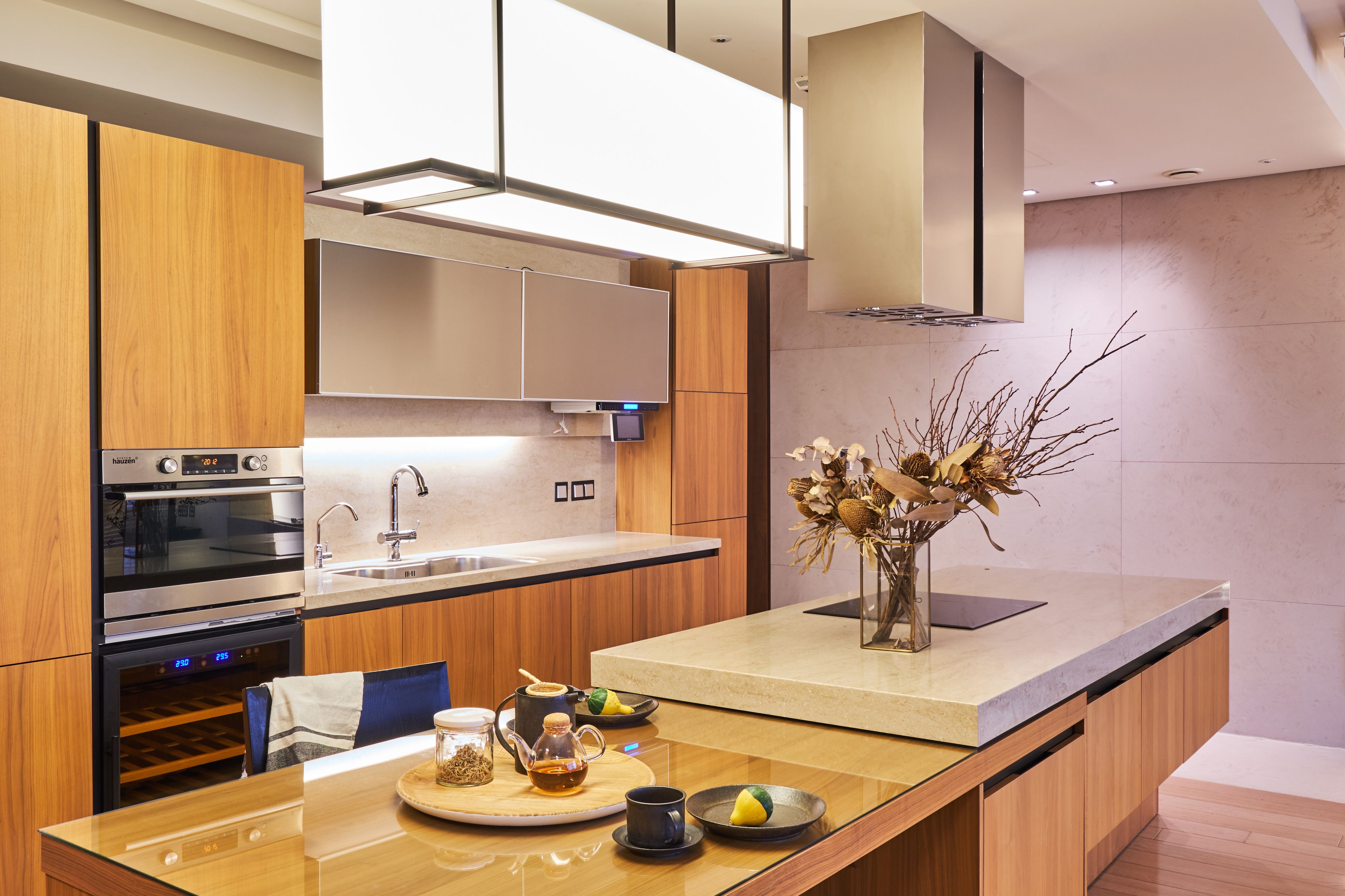 A modern kitchen with built-in appliances, a central island, and a vase with dried branches.