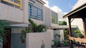 A modern building with a flat roof, multiple windows, and a small garden area with plants and a wooden bench.