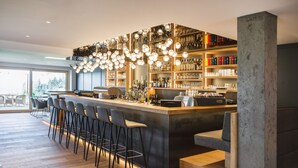 A modern bar area with a long counter, multiple stools, and a variety of bottles and glasses on shelves.