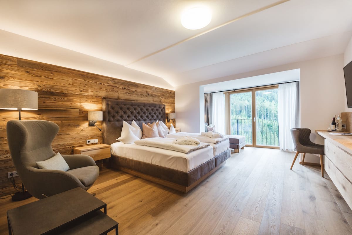 Een moderne slaapkamer met een groot bed, een houten accentmuur, een bureau en een stoel.