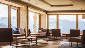 A spacious room with large windows, wooden walls, and a seating area with sofas and chairs.