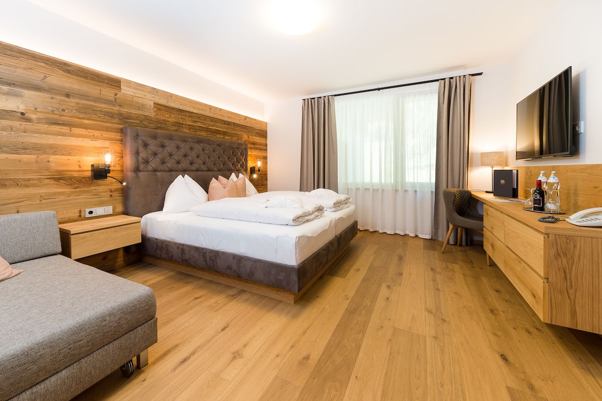 Een hotelkamer met een houten wand, een bed met witte lakens, een bureau met een flatscreen televisie en een bank.