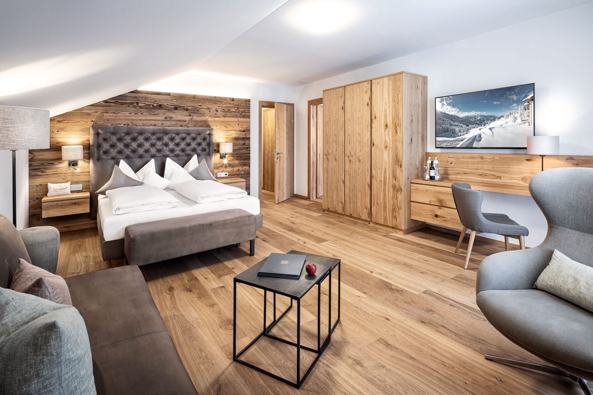 Een moderne slaapkamer met een groot bed, een bureau en een stoel. Er is een houten garderobe en een televisie aan de muur.