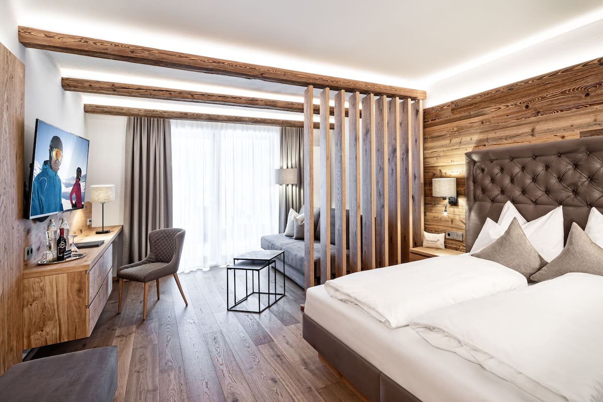 Een hotelkamer met een houten plafond, een groot bed met veel kussens, een bureau met stoel, een televisie en een raam met gordijnen.