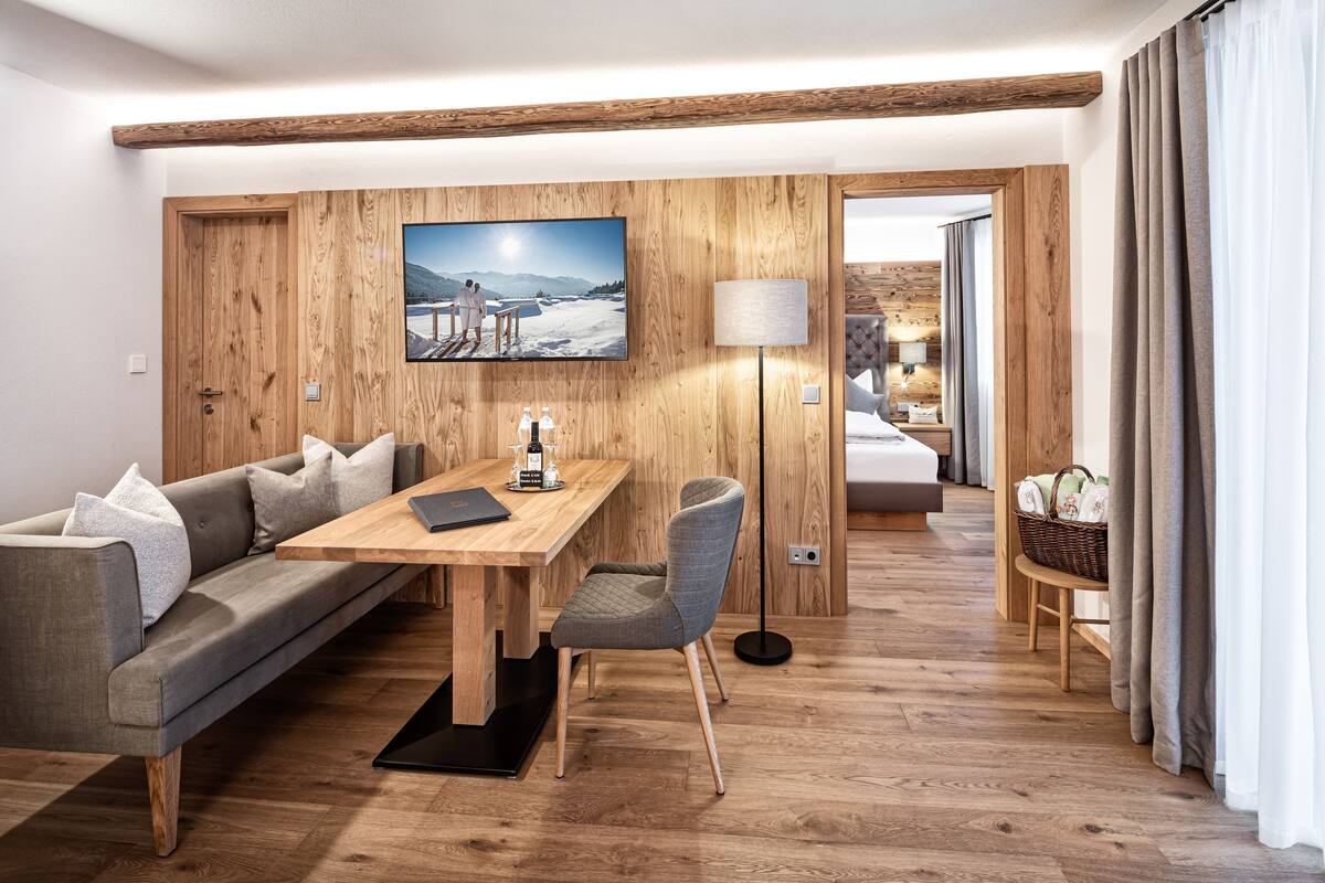 Een moderne hotelkamer met een wand van hout, een zithoek met een tafel en stoelen, een bank en een groot raam met gordijnen.