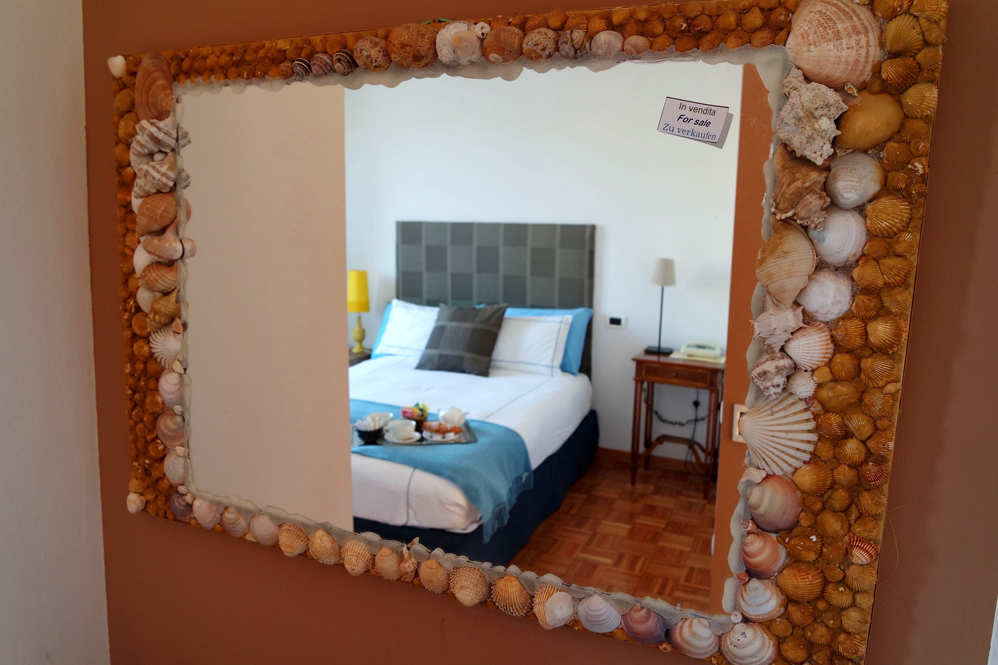 Une chambre à coucher comprenant un lit, une table de chevet, une lampe et un miroir orné d’un bord en forme de coquillage.