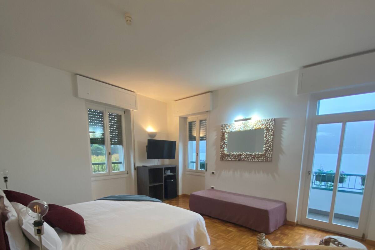 A bedroom with a large bed, a television, a wicker chair, and a balcony with a view.