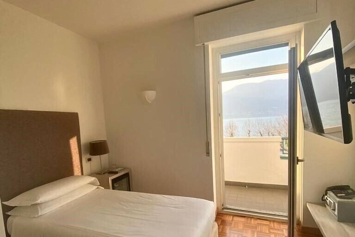 A hotel room with a bed, a nightstand, a desk, a mirror, and a view of the outdoors through a sliding door.