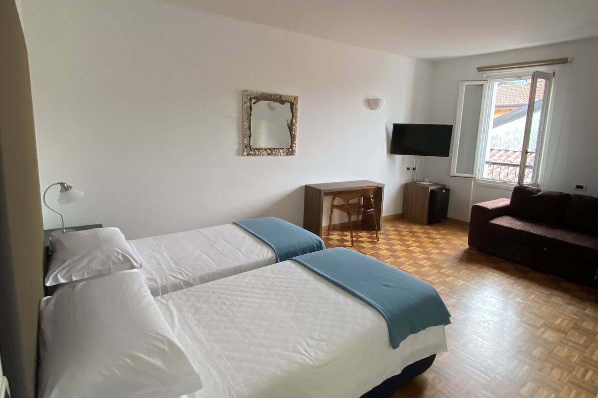 A bedroom with two beds, a desk, a TV, and a window.