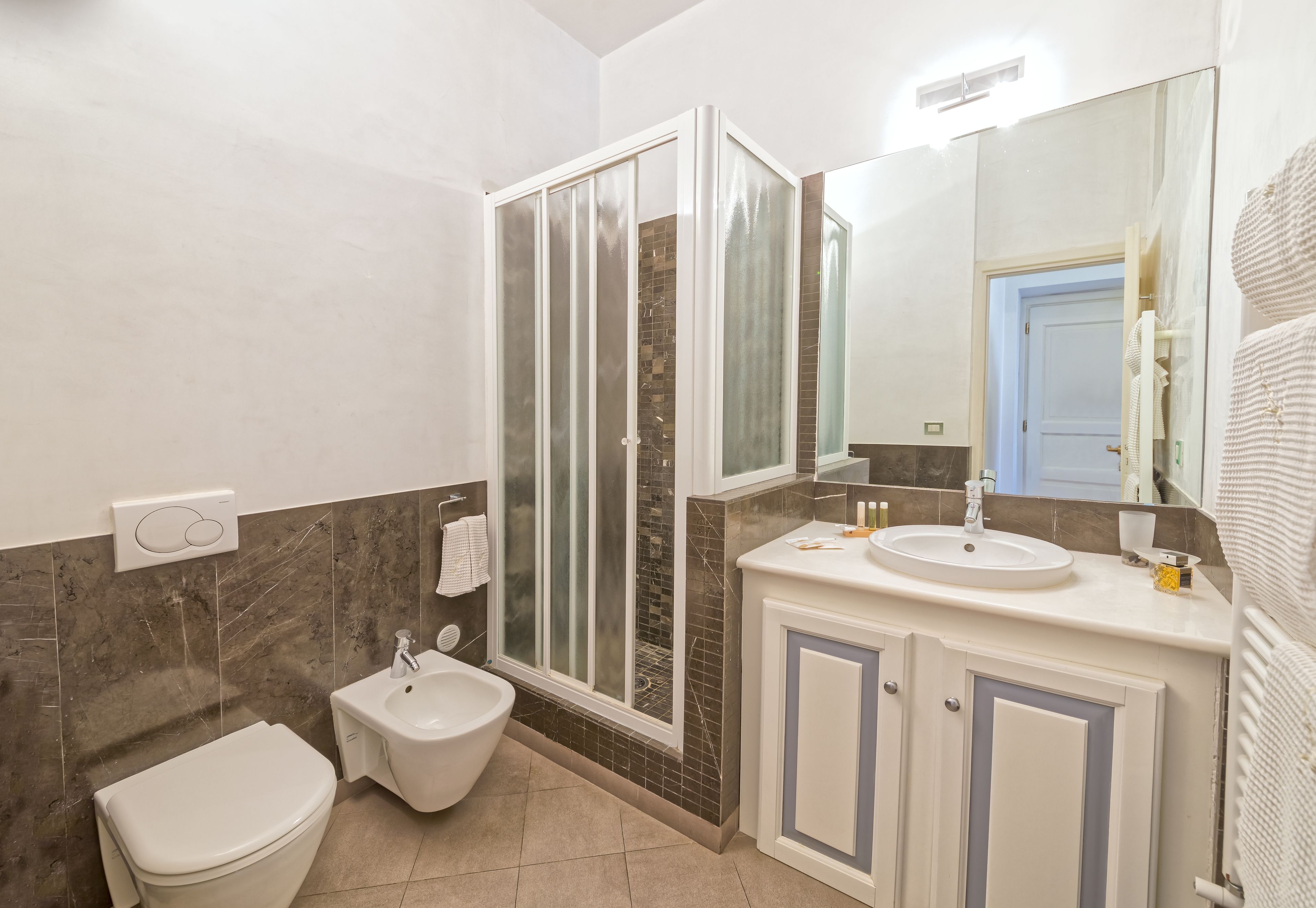 A bathroom with a toilet, bidet, sink, and a glass-enclosed shower.