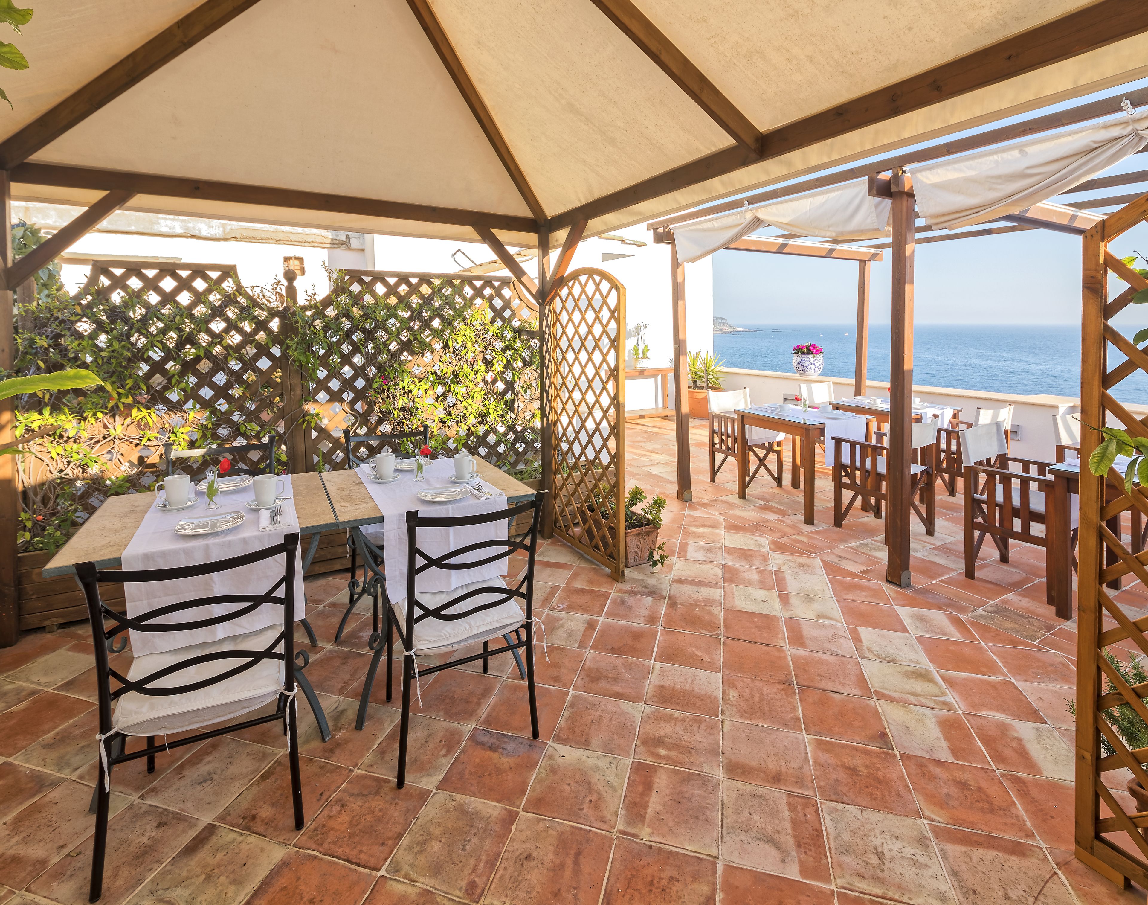 Une terrasse extérieure avec des tables et des chaises, une pergola en bois et une vue sur la mer.