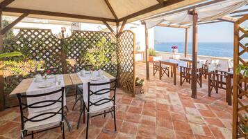Une terrasse extérieure avec des tables et des chaises, une pergola en bois et une vue sur la mer.