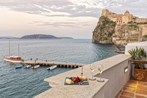 A terrace with a view of the sea, a dock with boats, and a historic building on a cliff. - Villa Lieta (Ischia)