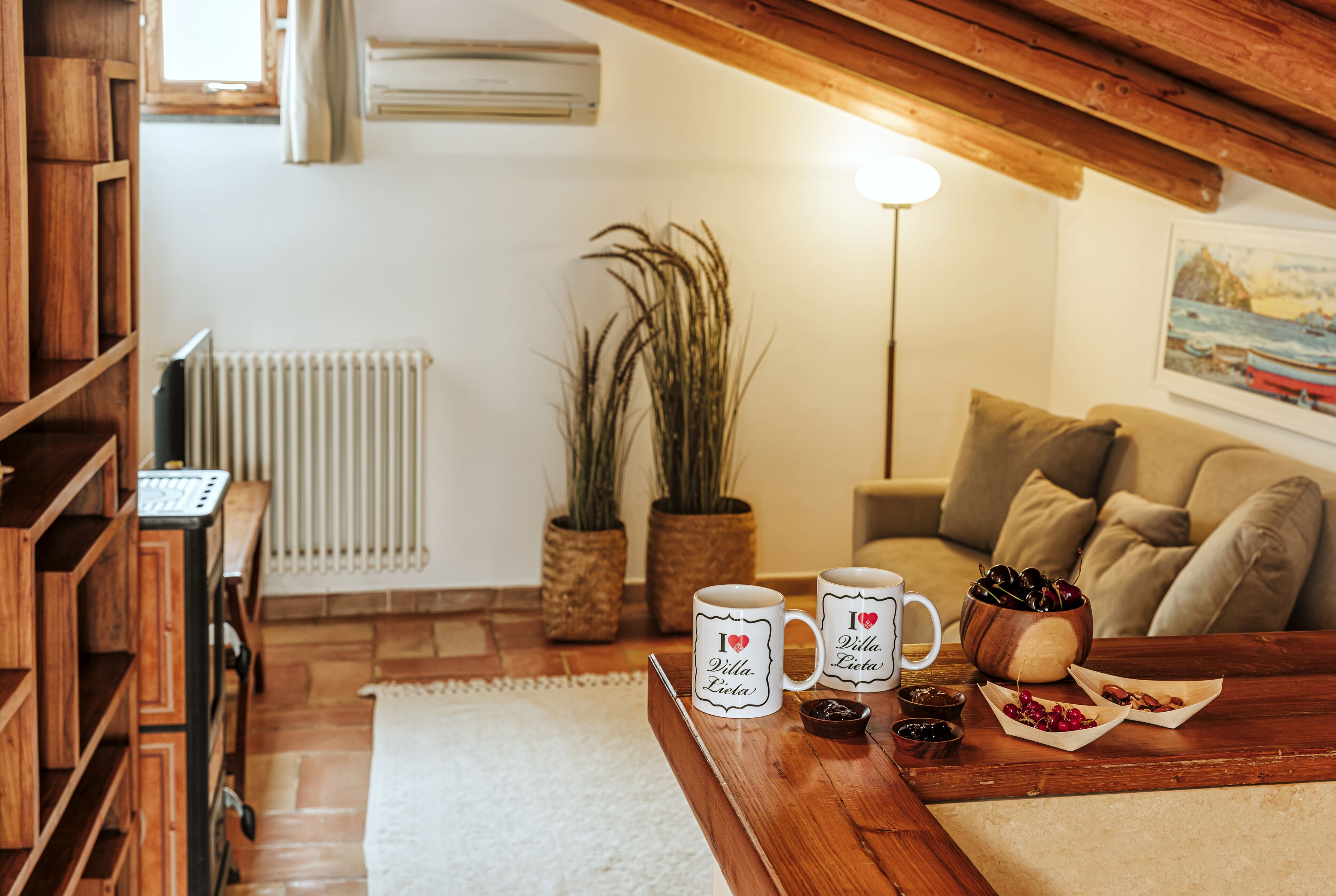 A cozy living room with a wooden coffee table, two white mugs, and a bowl of cherries.