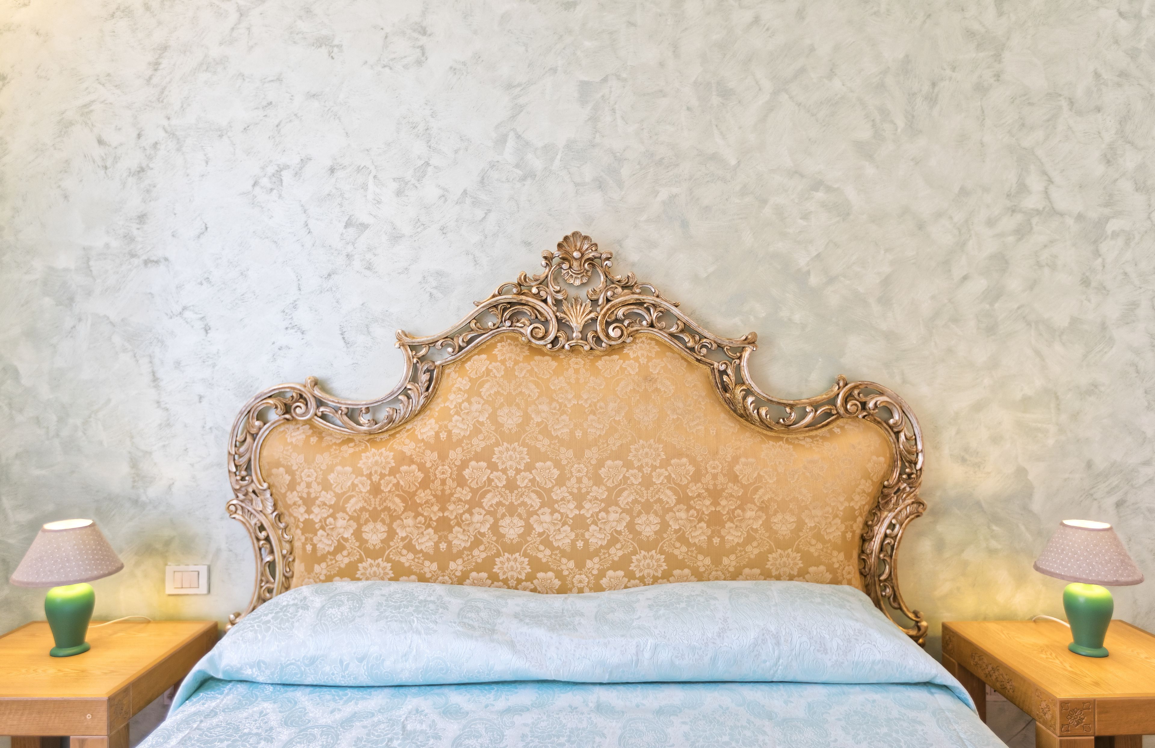A bedroom with a large ornate bed, two bedside tables with lamps, and a textured wall.