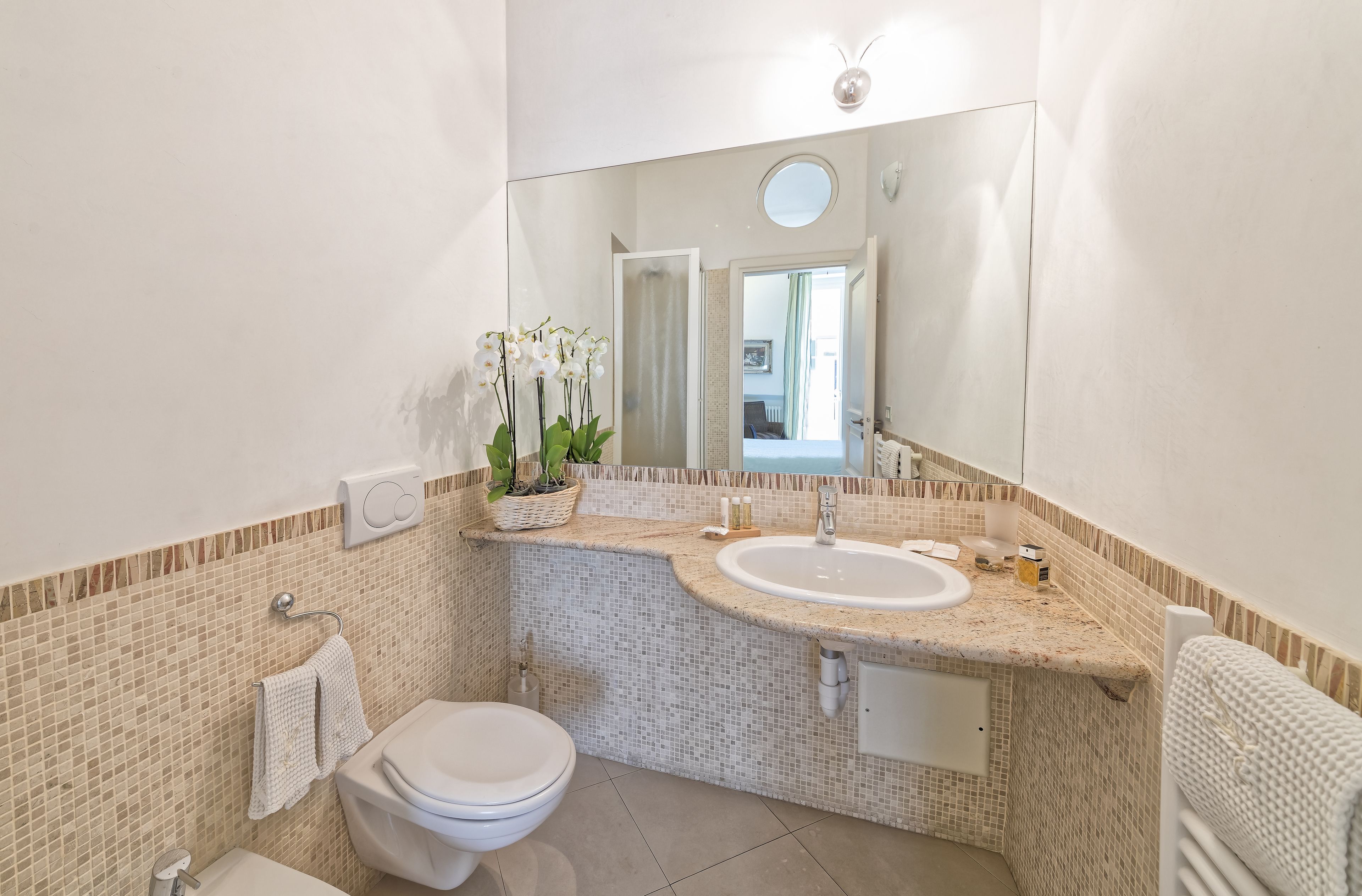 Un baño con inodoro blanco, dos lavamanos, un espejo grande y una orquídea en maceta.