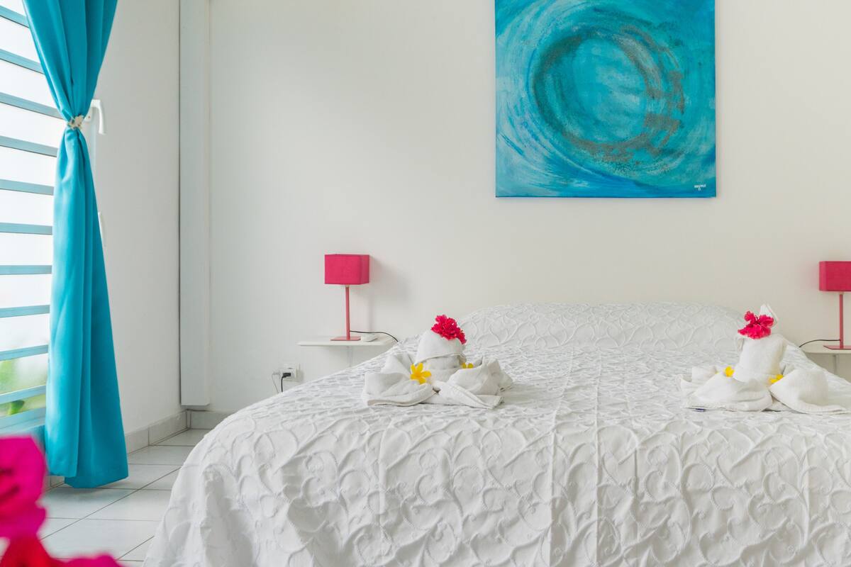 Habitación de hotel con una cama grande, dos mesitas de noche con lámparas, un cuadro en la pared y una ventana con cortinas.