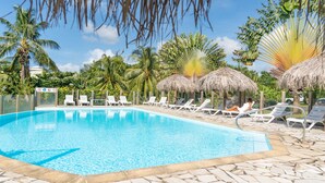 Uma piscina com espreguiçadeiras e guarda-sóis de palha.