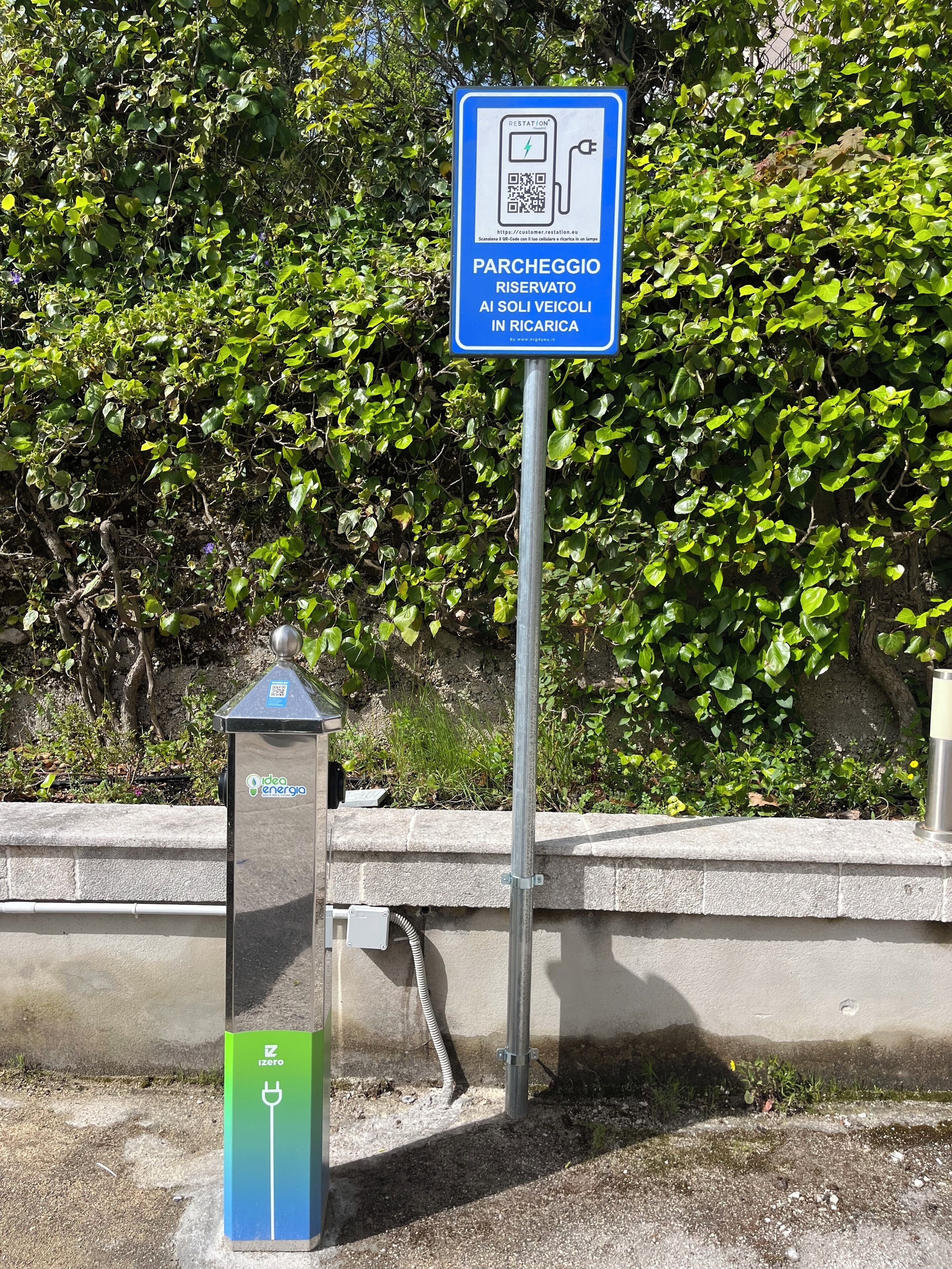 Un panneau de signalisation indiquant un espace de stationnement, doté d’un code QR et d’une borne de recharge.