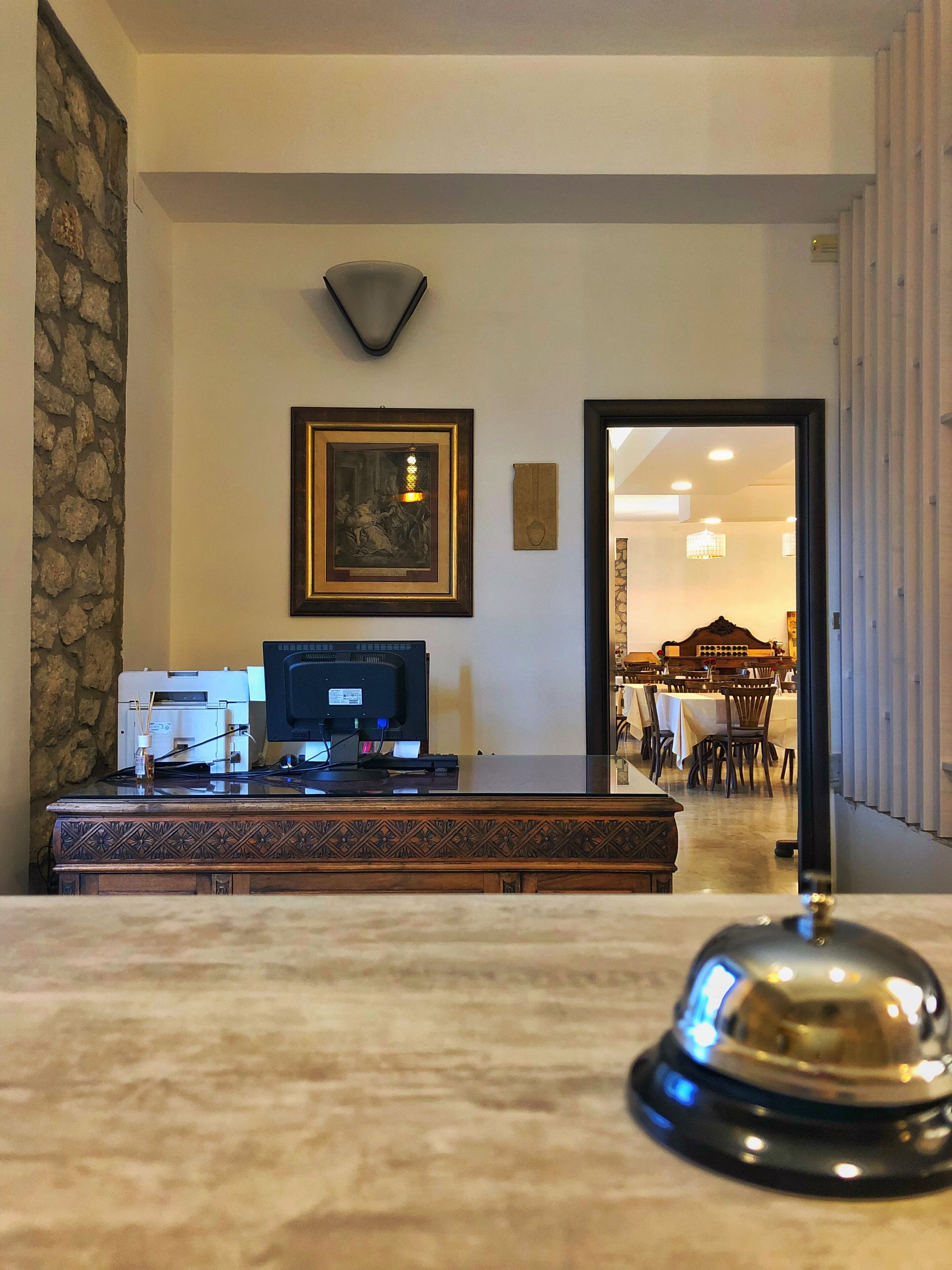 A reception area with a wooden desk, a framed artwork, a stone wall, and a view into a dining area.