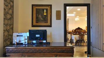 A reception area with a wooden desk, a framed artwork, a stone wall, and a view into a dining area.