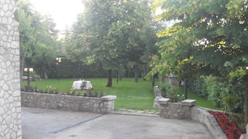 Un patio con suelo empedrado, muros de piedra y un césped con árboles.
