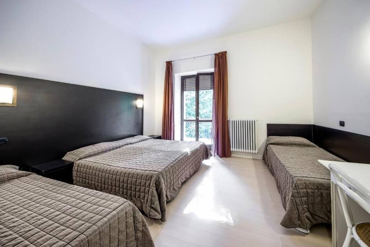 A hotel room with two beds, a desk, and a window with curtains.