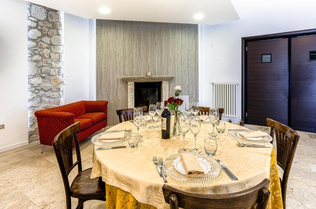 A dining room with a round table set for a meal, a fireplace, and a stone wall.