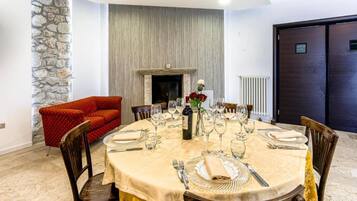 A dining room with a round table set for a meal, a fireplace, and a stone wall.