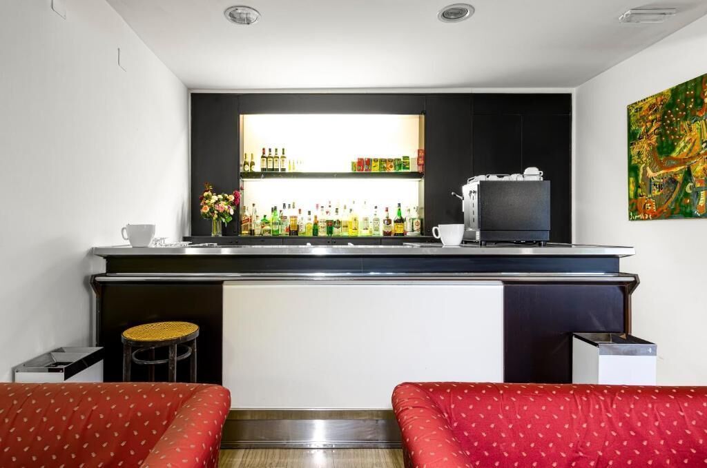 Cocina compacta con barra, cafetera y refrigerador. Hay dos taburetes y una mesa pequeña.