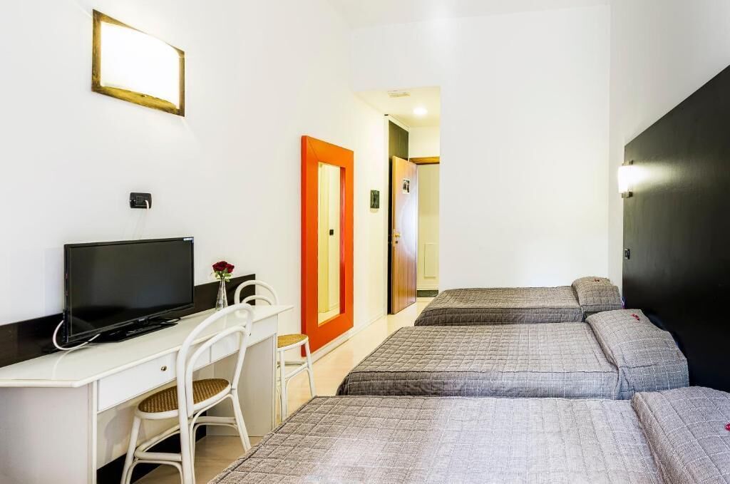 Une chambre d’hôtel équipée d’un bureau, d’une télévision, de deux lits et d’une porte avec un miroir.