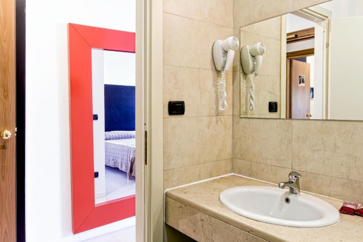 Een badkamer met een wastafel, twee haardrogen en een spiegel.
