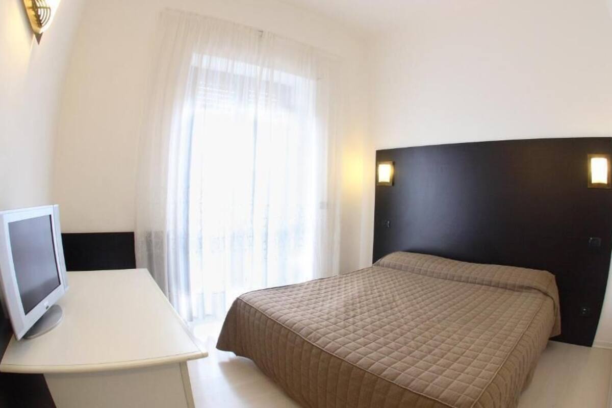 A hotel room with a bed, a desk with a computer, and a window with curtains.