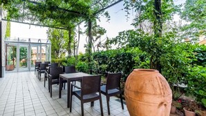 Un patio cubierto con suelo de baldosas, una mesa con sillas y una maceta de terracota grande.