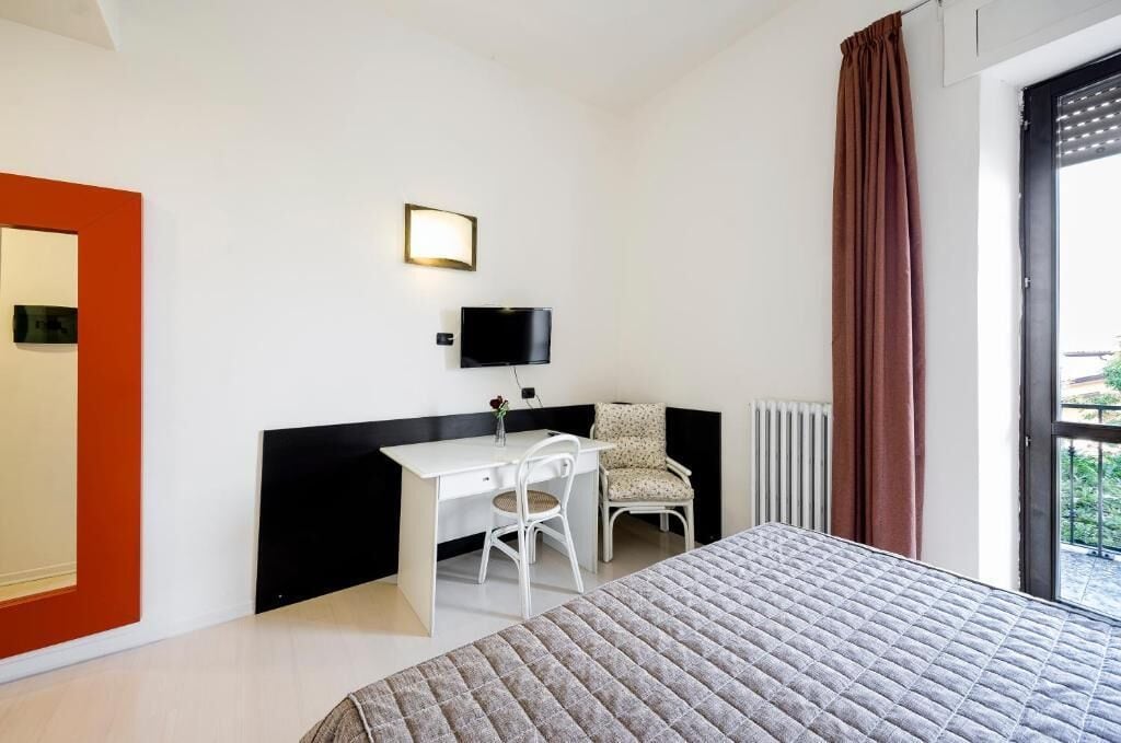 Ein Hotelzimmer mit einem Bett, einem Schreibtisch mit Stuhl, einem Fernseher und einem Fenster mit Vorhängen.