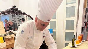 Un chef preparando comida en una cocina con una mesa de madera, una tabla de cortar y diversos utensilios de cocina.