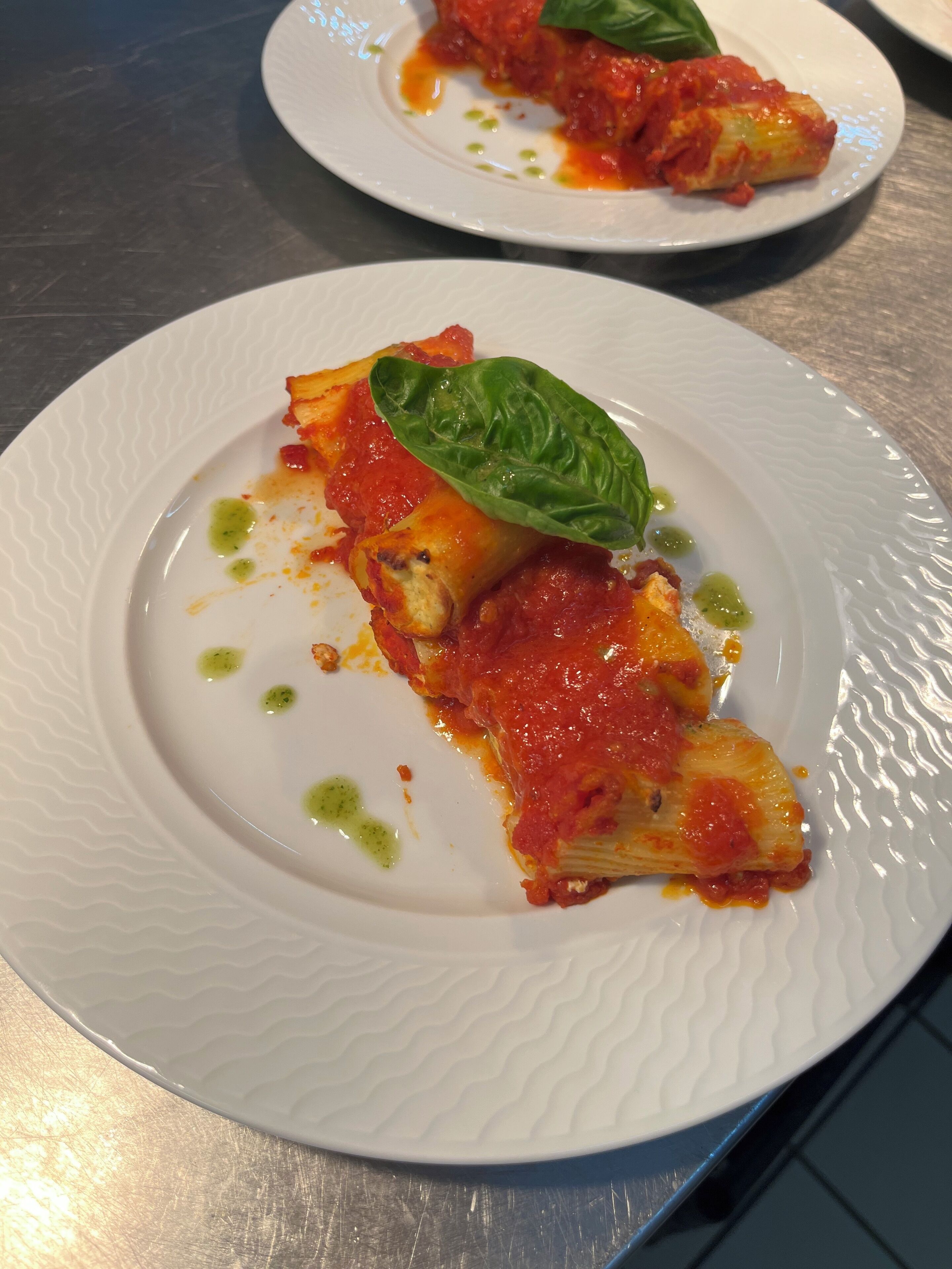 Een bord met een plak pizza, belegd met tomatensaus en kaas, versierd met een basilicumblaadje.