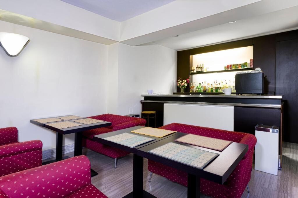 Quarto de hotel com área de bar, assentos estofados em vermelho e um pequeno frigorífico.