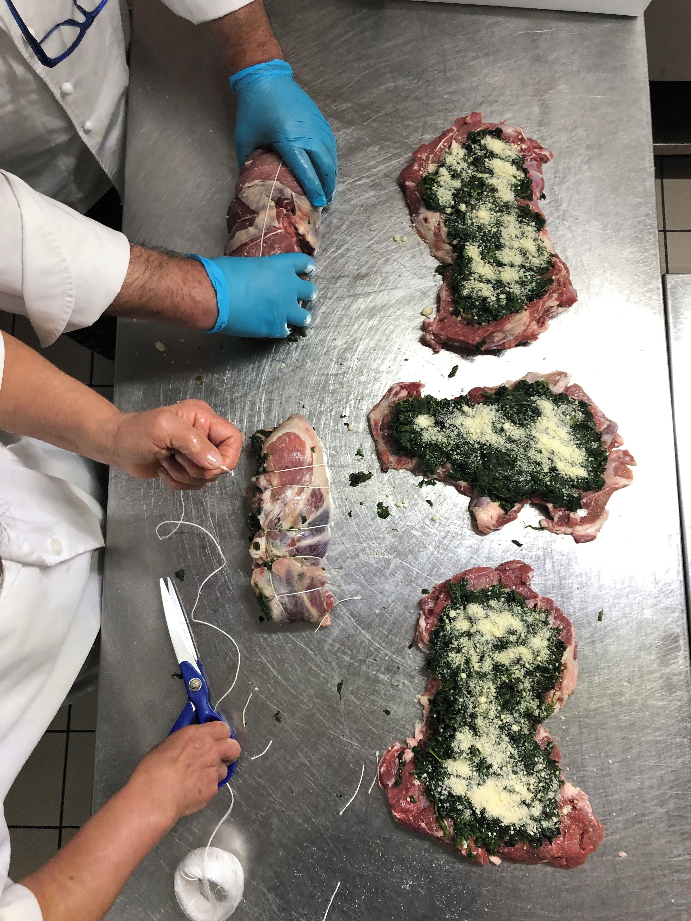 A person preparing meat with a knife and scissors on a stainless steel surface.