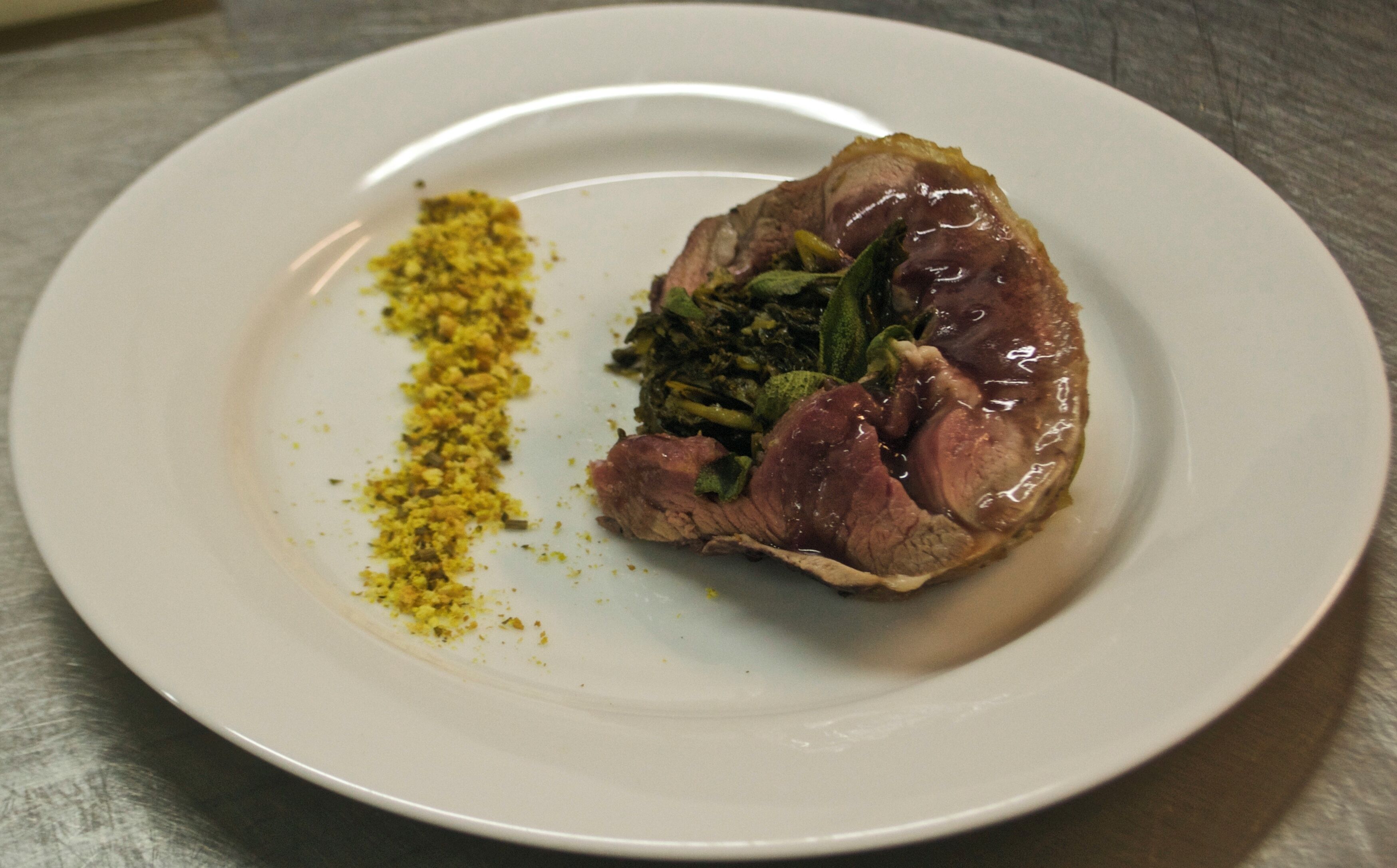 A plate with a piece of meat, greens, and a yellow spice.