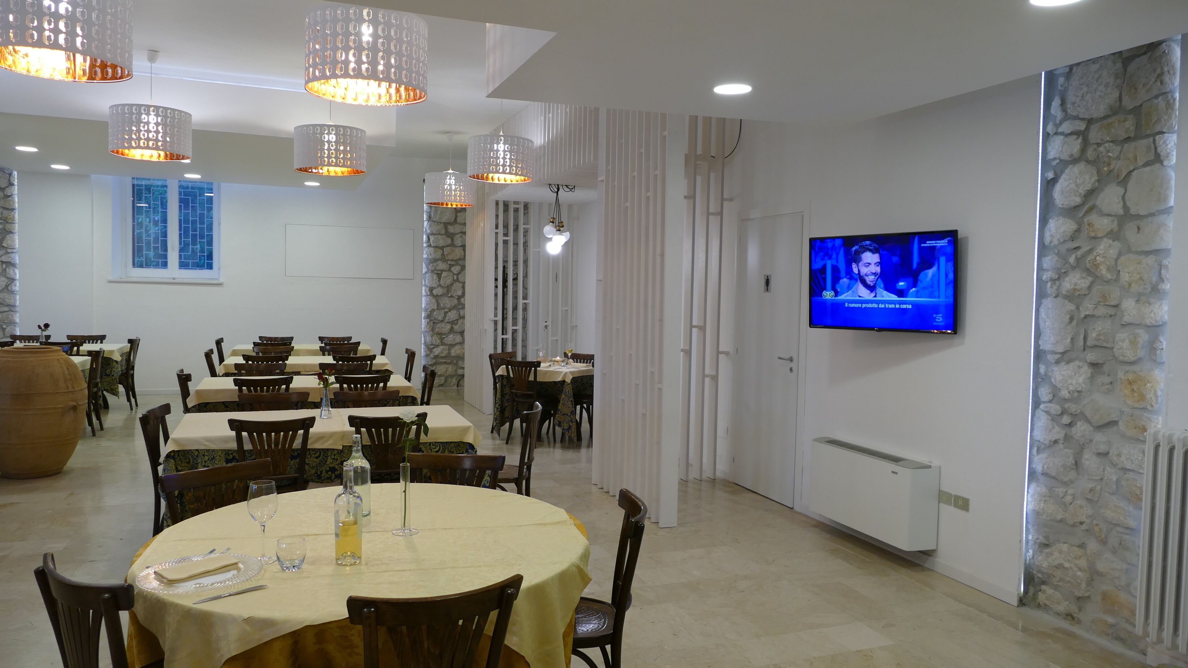 A dining area with multiple tables and chairs, a television mounted on the wall, and a stone accent wall.