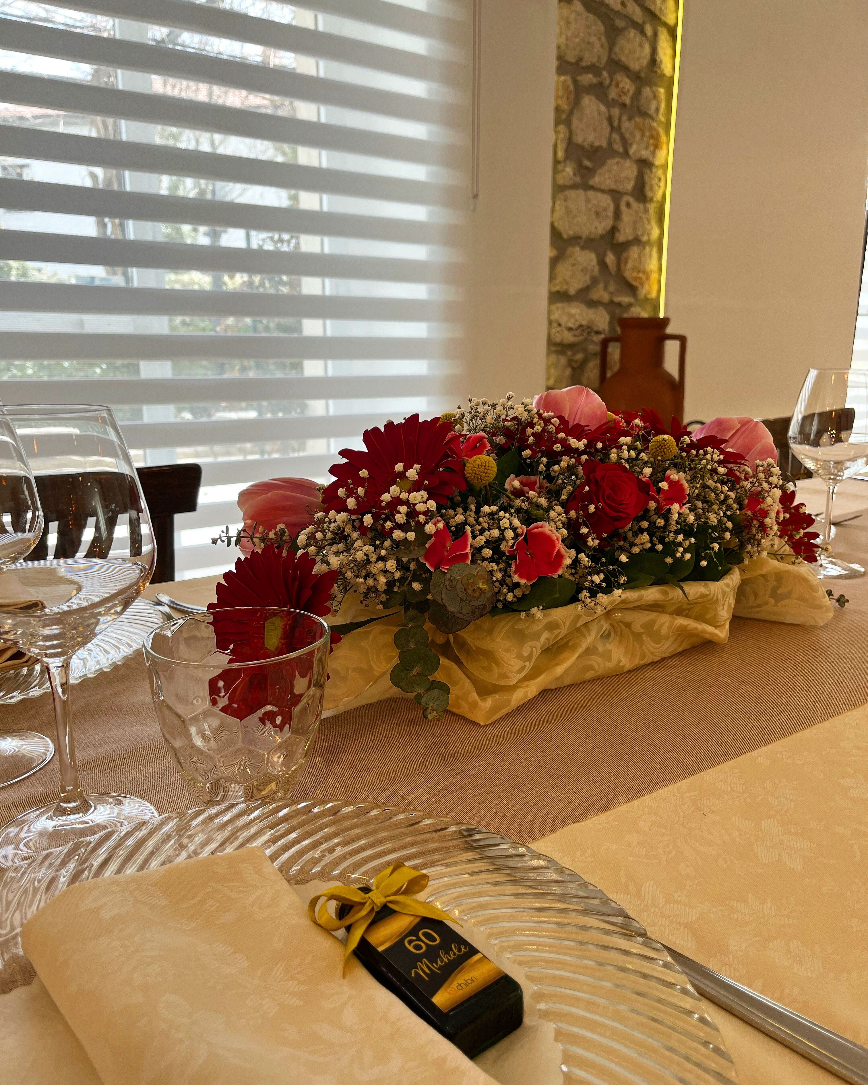 Ein Tisch gedeckt mit Weingläsern, einer Zierblumenkomposition und einer Geschenkbox.