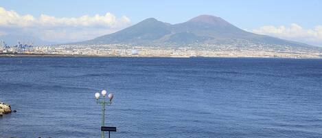 A waterfront promenade with a view of a mountain, a cityscape in the background, and a few people walking along the path.