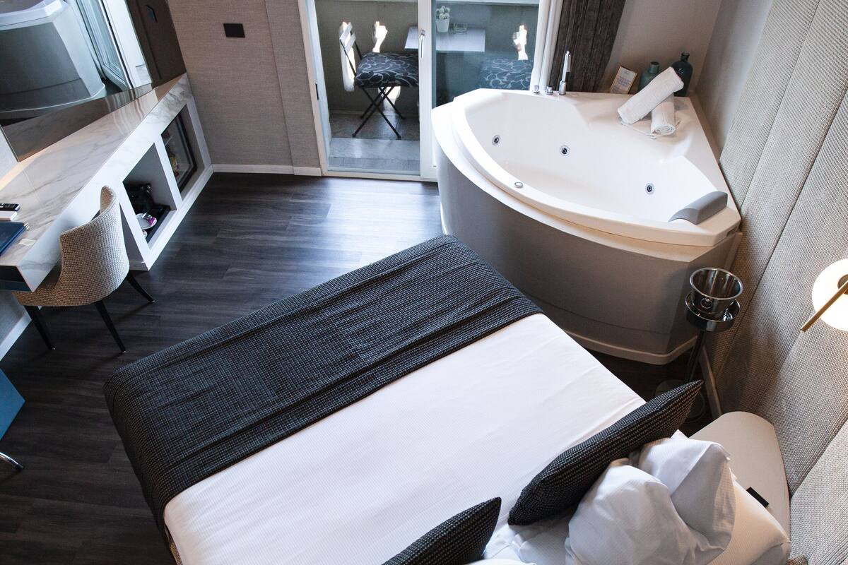 Une chambre d’hôtel moderne dotée d’un grand lit, d’un coin salon avec un fauteuil, d’un bureau et d’une baignoire.