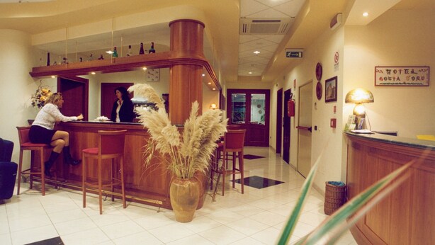 A hotel lobby with a reception desk, wooden chairs, and a large vase with pampas grass. - Hotel Costa d'Oro (Salve)