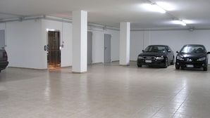 Un garaje para coches con dos vehículos estacionados, paredes blancas y suelo de baldosas.