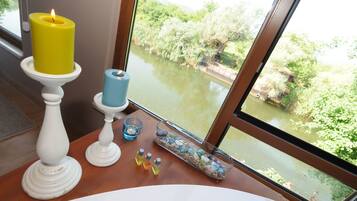 Un baño con un ventanal grande, una vela amarilla sobre un pedestal blanco, una vela azul y un recipiente de vidrio con piedras y una vela azul.