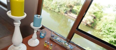Un baño con un ventanal grande, una vela amarilla sobre un pedestal blanco, una vela azul y un recipiente de vidrio con piedras y una vela azul.